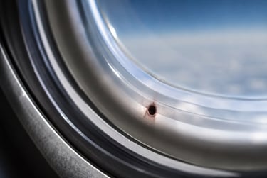 Close-up of a small breather hole in an airplane window overlooking clouds.