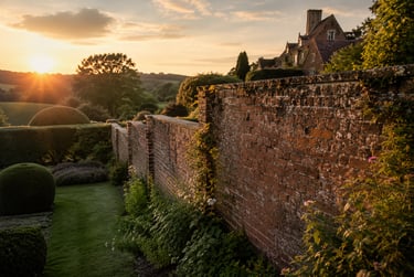 A golden sunset over a traditional English country estate garden with a brick wall and manicured hedges.