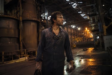 A gritty industrial worker in a dark steel mill wearing blue overalls and safety goggles.