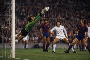 A soccer goalkeeper in a green jersey jumps to catch the ball during a professional match.