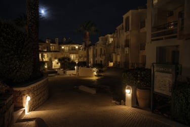 Night view of a luxury ocean club resort with lit stone pathways, white buildings, and a full moon.
