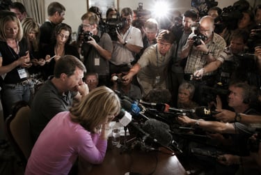 A crowd of journalists and news photographers with cameras surrounding a couple at a press conference.