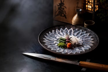 Thinly sliced fugu pufferfish sashimi arranged on a platter with a Japanese yanagiba sushi knife and sake.