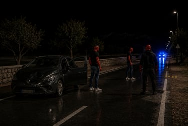 Forensic investigators in red suits examine a night car accident scene with police lights.