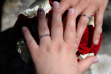 Mains des mariés avec leurs alliances sur fond de bouquet de fleurs
