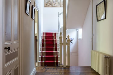 Élégant intérieur de maison avec escalier recouvert d’un tapis rouge, rampe blanche et parquet.