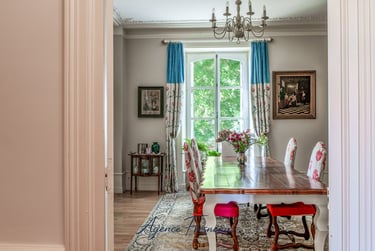 Élégante salle à manger avec table en bois, chaises à motifs floraux et rideaux bleus à proximité d’