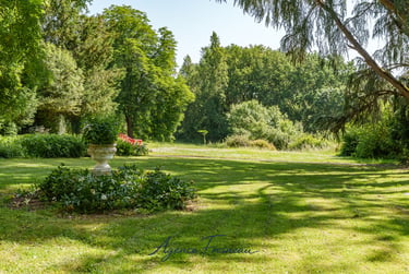 Urne de jardin en pierre dans un parc paysager, entourée de pelouse et de végétation.