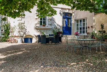 Cour intérieure de villa en pierre de prestige avec porte bleue, mobilier de terrasse et jardin.