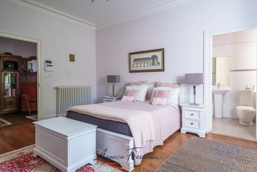 Élégante suite parentale avec linge de lit rose, mobilier blanc et salle de bains attenante