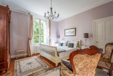 Élégante chambre de style campagne française avec lit en bois blanc, fauteuils vintage et lustre.