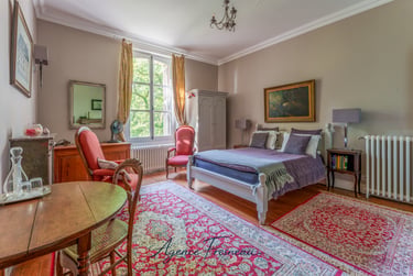 Élégante chambre de style classique avec lit en bois, tapis rouges à motifs et mobilier français.