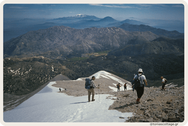 Hikers on a snowy trail in the Crete mountains during winter, with snow-covered peaks and blue skies