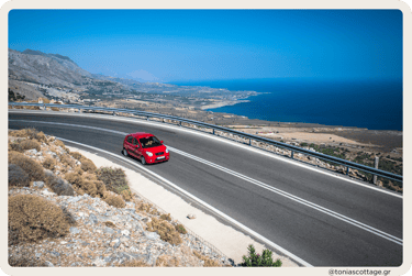 A red rental car driving down a winding road in Crete, Greece, surrounded by beautiful scenery