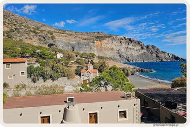 Koudoumas Monastery perched on rolling hills surrounded by green shrubland and dry rocky terrain.