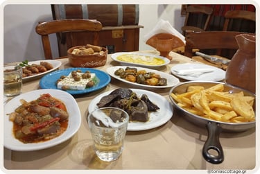 Cretan meze feast with fries, feta, beans, stewed meat, and raki shots on a wooden table