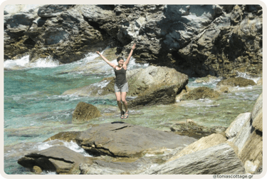 Tonia with raised arms standing on coastal rocks by clear turquoise sea in Crete
