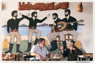 Two men sitting in a kafenio, talking, drinking coffee, with Cretan dancers painted on the wall