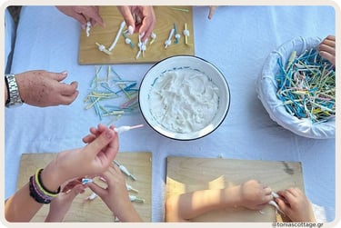 Top-down view of hands dipping colorful wooden sticks into a bowl of white sweet syrup in Crete