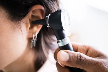 A doctor performing an ear exam on a patient using a black otoscope tool.