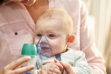 Mother holding baby using a nebulizer face mask for respiratory treatment of asthma or cold symptoms.