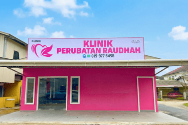 Pink storefront of Klinik Perubatan Raudah medical clinic with large signage under a blue sky.