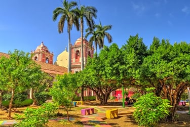 Sunny park in Leon, Nicaragua, featuring tropical palm trees and a historic colonial church under a blue sky.