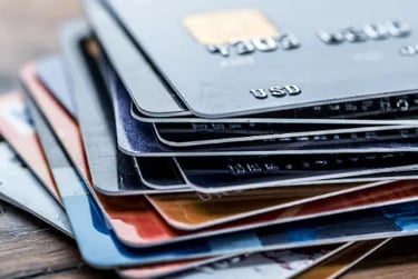 A close-up stack of multiple plastic credit cards and debit cards on a wooden surface.