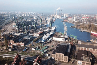 Aerial view of an industrial shipyard with large green cranes and ships along the city waterfront.