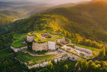 Aerial view of a historic star-shaped stone fortress nestled in lush green mountain hills at sunset.