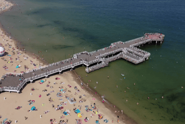 Aerial view of a crowded sandy beach and wooden pier extending into the Baltic Sea.