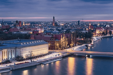Panoramic aerial view of Wroclaw, Poland, at dusk, showcasing the illuminated historic architecture along the Oder River and
