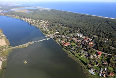 Aerial view of a coastal village nestled between a calm bay and a lush green forest by the blue sea.