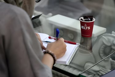 Person writing in a notebook, symbolizing IELTS preparation with U.E.L.T's cup for studying abroad