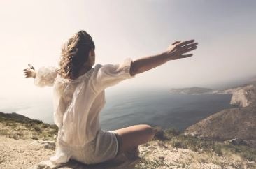 Femme assise face à la mer, bras ouverts, illustrant la libération des addictions