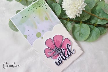 Greeting card with pastel watercolor background and "Bloom a little wild" sentiment