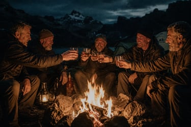 A group of male friends toasting with whiskey glasses around a warm campfire while mountain camping at night.