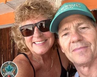 Jo Schultz smiling, wearing sunglasses hugging behind her husband