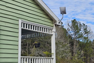 A Starlink satellite dish mounted on the roof of a green house with a white porch railing.