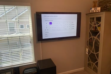 A wall-mounted smart TV displaying a digital keyboard for email login in a home office.