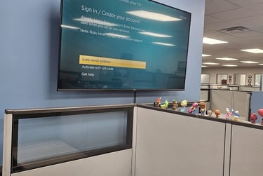 Hisense Roku TV mounted on a blue office wall showing a sign-in activation screen above office cubicles.