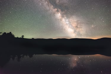 Vibrant Milky Way galaxy reflecting in a calm lake with mountain silhouettes under a starry night sky.