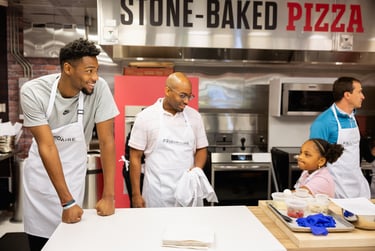 Smiling group wearing Frigidaire aprons in a stone-baked pizza kitchen during a cooking class.
