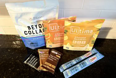 Collagen, protein snacks, RXBARs, beef sticks, and electrolytes arranged on the kitchen counter