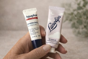 Hand holding Aquaphor Lip Repair and Lanolips Overnight Lip Mask against a soft neutral background