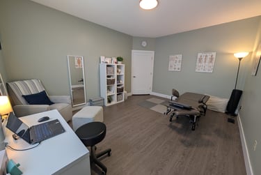 Professional pelvic physiotherapy room featuring pelvic health table, anatomical posters, desk.