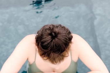 A woman in a green swimsuit resting her arms on the edge of a cold plunge pool at Saltair Nordic Spa