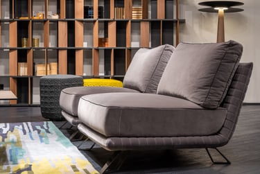 Modern grey velvet lounge chair in a luxury living room with a wooden bookshelf and colorful area rug.