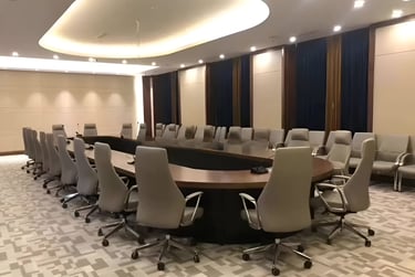 Modern corporate conference room with a large oval boardroom table and gray ergonomic chairs.