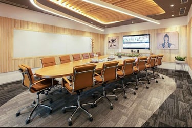 Modern conference room with tan leather chairs, a long oval wooden table, and wood-paneled walls.